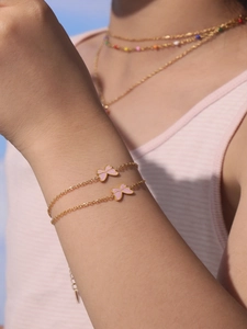 Close-up of golden link bracelet featuring pink butterfly charms worn on a model's wrist