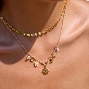 Dettaglio di collane a strati con ciondoli a forma di sole e fiori placcati oro 18K