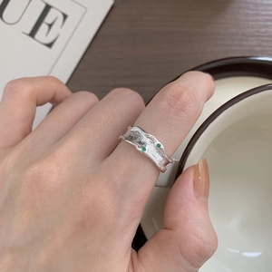 Detailed view of an irregular silver ring with green gems on a textured surface