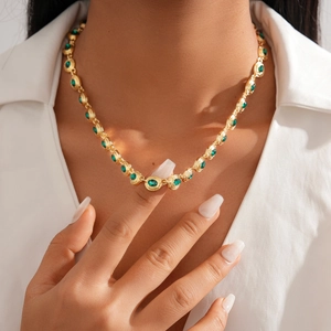 Close-up of vintage gold necklace with green oval rhinestone on a white shirt