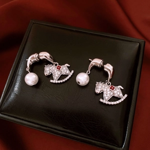 Détail de boucles d'oreilles cheval à bascule argentées avec perles et fleurs rouges