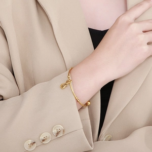 Detail of a gold violin charm on a sleek metal bangle worn with a beige business suit