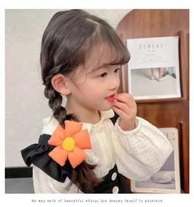 Detailed view of an orange fabric sunflower hair tie worn by a toddler on a ponytail
