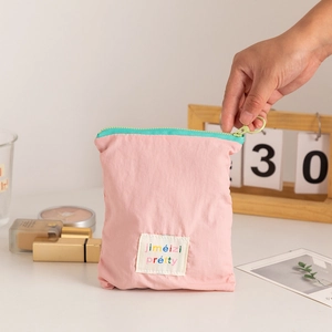 Pink fabric cosmetic bag with mint green zipper and decorative woven label detail