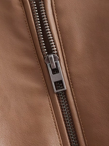 Detailed macro shot of brown leather jacket with matte metal zipper and fine stitching