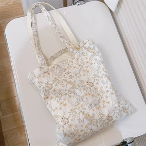 Detailed view of floral canvas tote bag with rabbit illustrations on white surface