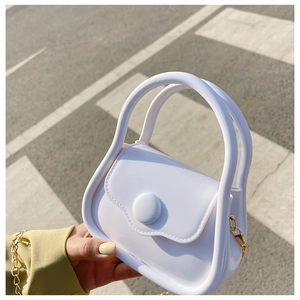 Outdoor shot of a white mini jelly bag featuring a golden chain strap on a zebra crossing