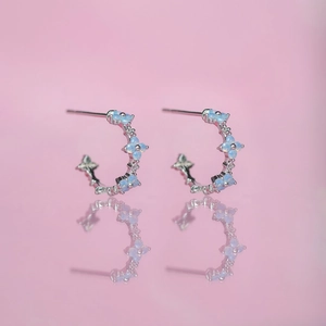 Blue zircon flower hoop earrings in silver finish on pink background with reflection