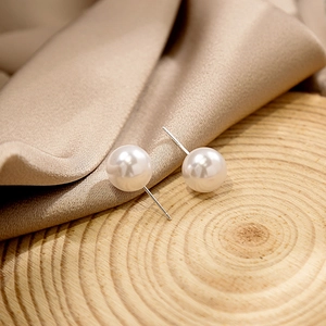 Macro shot of elegant white pearl earrings on wood base with champagne silk background