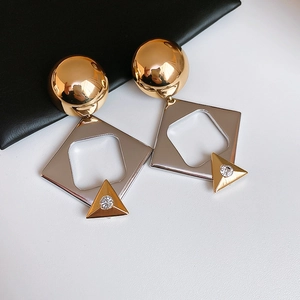 Close-up of geometric earrings with gold spheres, silver diamonds, and crystal studs