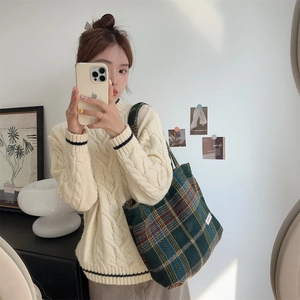 Detail shot of green plaid wool tote bag styled with a cream cable knit sweater