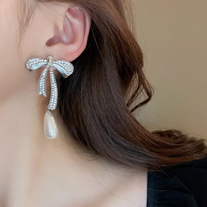 Close-up of elegant silver bow earrings with drop white pearls worn by a model