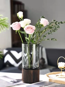 Close-up of a clear cylindrical glass vase on a dark wood base with pink roses