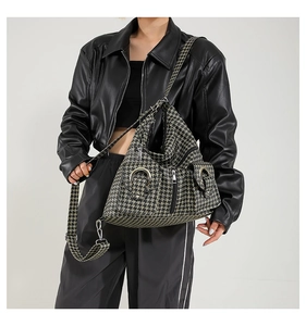 Detail view of large houndstooth crossbody bag featuring metal rings and zip pockets