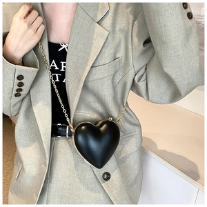 Detail of a black heart-shaped crossbody bag with a gold chain on a light green suit