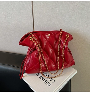 Detail of red quilted bucket bag with elegant gold chain strap and diamond pattern