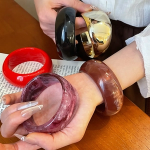 Macro shot of wide chunky resin bangles in solid colors and marble textures on wood