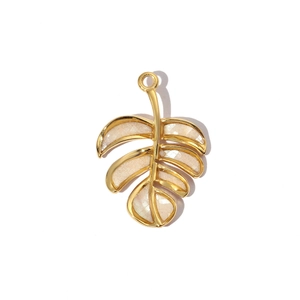 Detailed view of a gold tropical leaf pendant with cream enamel inlay on white background