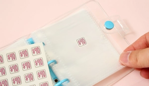 Detail of transparent PVC binder with blue rings and hand inserting a $40 savings sticker