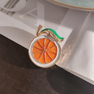 Macro view of slice orange enamel brooch with golden metal edges and green leaf detail