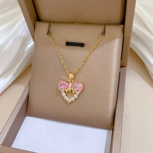 Detailed macro of pink gemstone bow and heart pendant on a gold necklace in gift box