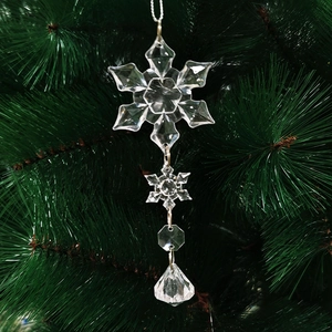 Close-up of clear acrylic snowflake and drop pendants hanging on green Christmas tree branches