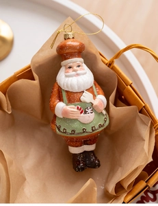 Close-up of a resin gingerbread Santa Claus chef ornament with green apron and gold cord