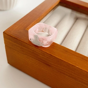 Detailed macro view of pink resin square ring with heart charm on a wooden jewelry box