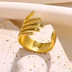 Detailed close-up of a golden hand-shaped open ring placed on a textured beige stone