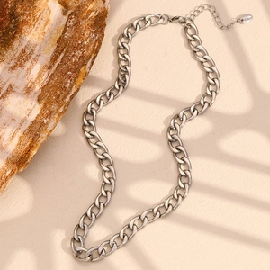 Detailed close-up of a silver-tone curb chain necklace on a minimalist stone background