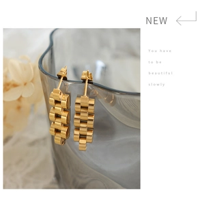 Detailansicht goldener Ohrringe im Uhrenarmband-Stil an einem Glas mit Trockenblumen