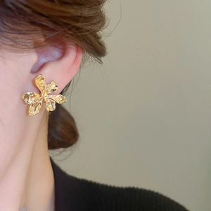 Close-up of golden metal flower earring with textured petals and elegant matte finish