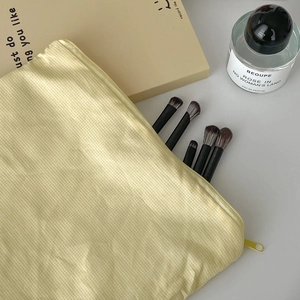 Yellow gingham makeup bag with brushes and perfume on a minimalist desk surface