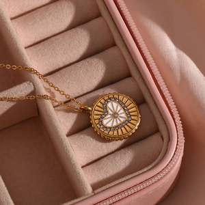Détail d'un collier pendentif pièce dorée avec cœur blanc et zircons dans une boîte rose