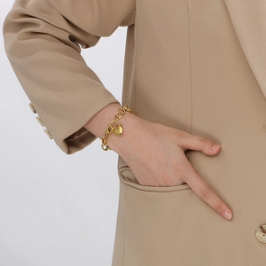 Detailed close-up of a chunky gold link chain bracelet with a heart pendant on a wrist