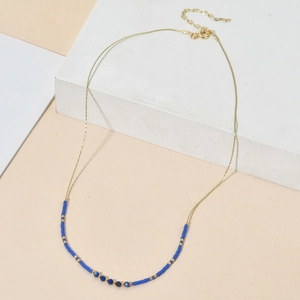 Gros plan d'un collier en chaîne dorée avec perles de cristal bleu sur support blanc