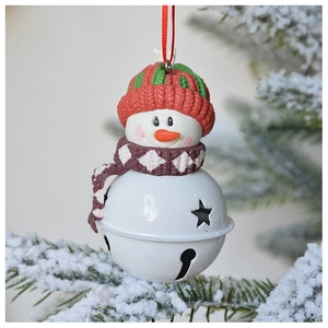 Close-up of a snowman metal bell ornament hanging on a snowy Christmas tree branch