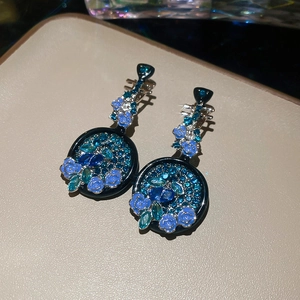 Dettaglio macro di orecchini a forma di pipa con rose blu, strass e smalto stile vintage