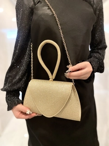 Detail of a gold glitter evening clutch bag with circular handle and metal chain strap