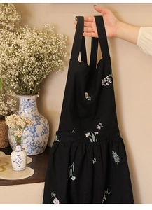 Detail of black cotton linen apron featuring exquisite floral embroidery and waist pleats