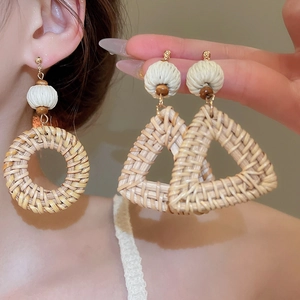 Detail of woven rattan geometric earrings with white cotton balls and wooden beads