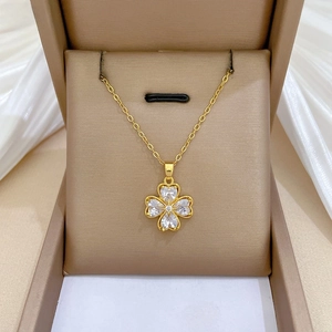 Close-up of gold clover necklace with heart-shaped crystals displayed in a gift box