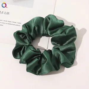 Macro shot of dark green silk satin scrunchie with elegant folds and glossy texture