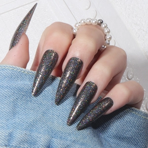 Macro shot of long stiletto false nails featuring dark holographic glitter on denim fabric