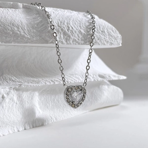 Macro shot of a silver heart pendant necklace featuring zircon stones on white stone background