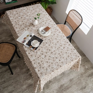 Detail of beige cotton linen tablecloth featuring floral patterns and delicate tassels