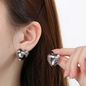 Detailed view of silver puffed heart earrings with hammered metal texture on ear