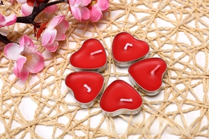 Five heart-shaped red tea light candles in silver aluminum shells on a woven mat base
