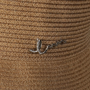 Close-up of stylish straw sun hat with silver metal letter emblem and crystal accents