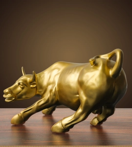 Detailed close-up of a dynamic golden bull sculpture with muscle lines on wood base